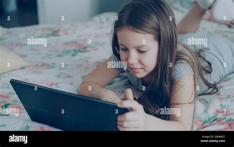 Cute little girl using digital tablet and smiling while lying in bed ...