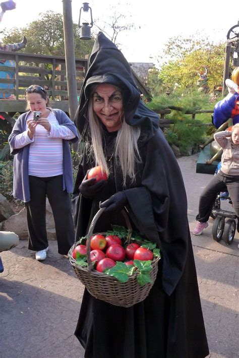 a woman dressed as a witch holding a basket of apples and vegetables in her hands