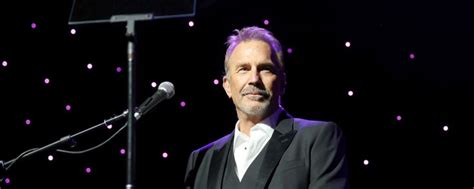 a man standing in front of a microphone at a podium with lights on the wall behind him