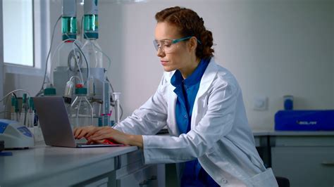 Female scientist working in laboratory. Lab worker typing test report on computer. Scientist ...