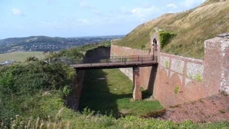 an old bridge on the side of a hill with hills in the background and grass growing all around