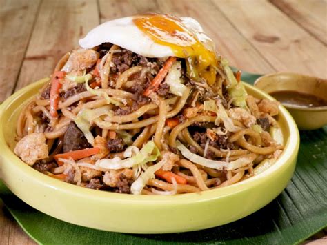 a yellow bowl filled with noodles, meat and an egg sitting on top of a green plate