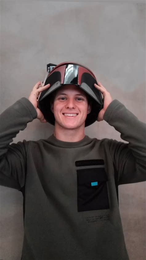 a young man wearing a helmet and holding his hands to his head while smiling at the camera