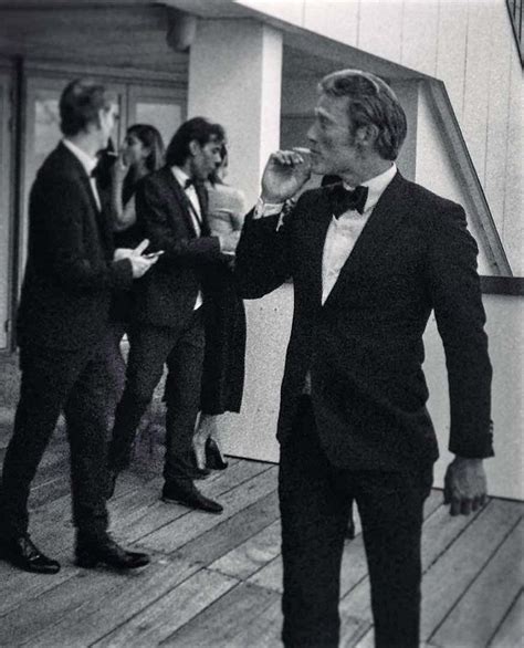 a man in a tuxedo is drinking from a glass while others look on