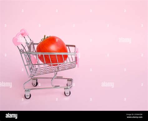 Small grocery cart with big unusual tomato on pink background Stock Photo - Alamy