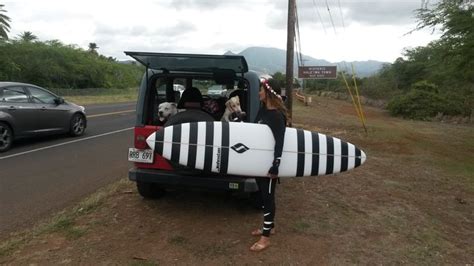 a woman holding a surfboard while standing next to a car on the side of the road