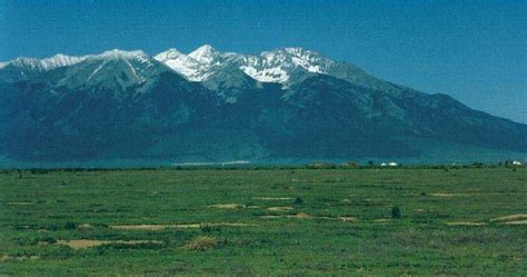 an open field with mountains in the background and snow on the top of ...