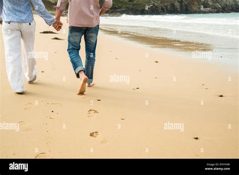 Cropped shot of mature couple holding hands whilst strolling on beach ...