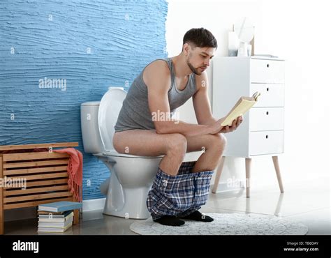 Man reading book while sitting on toilet bowl at home Stock Photo - Alamy