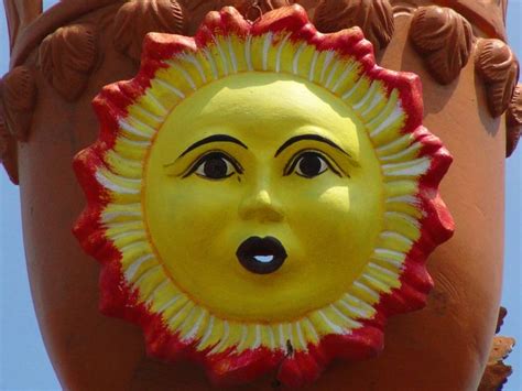 a yellow and red sun face hanging from the side of a large clay planter