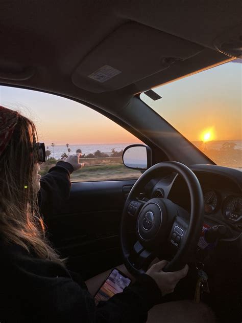 a woman driving her car at sunset with the sun setting in the distance behind her