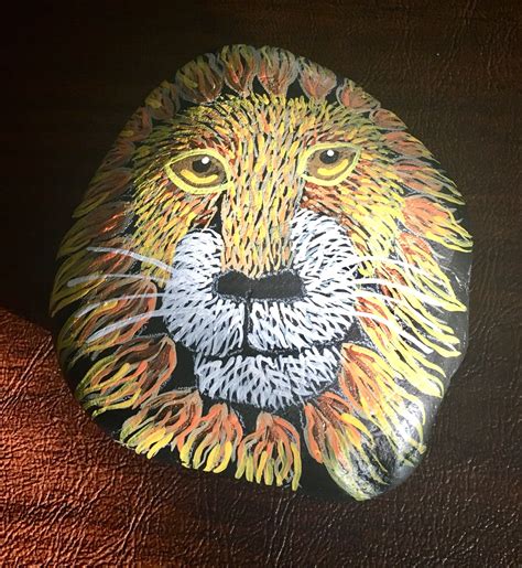 a painted rock with a lion's face on it sitting on a leather surface