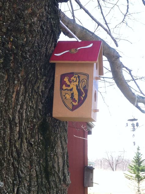 a birdhouse hanging from the side of a tree in front of a house with a coat of arms on it