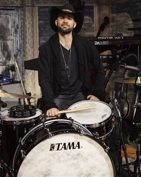 a man with a hat on sitting in front of a drum set