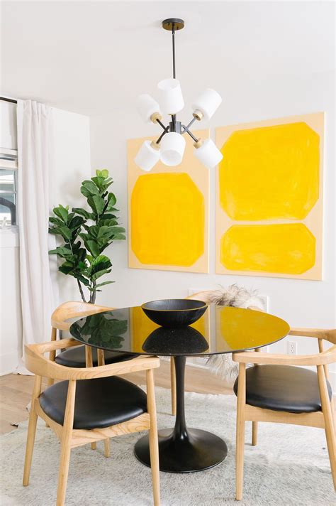 a modern dining room with yellow and black art on the wall above the glass table