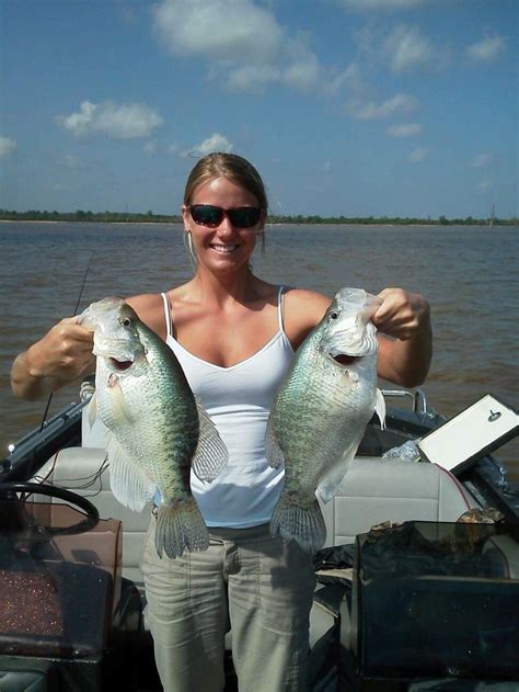 a woman holding two large fish on a boat in the middle of a body of water