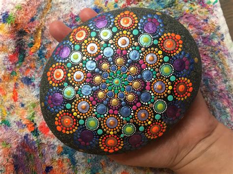 a hand holding a painted rock in the shape of a flower