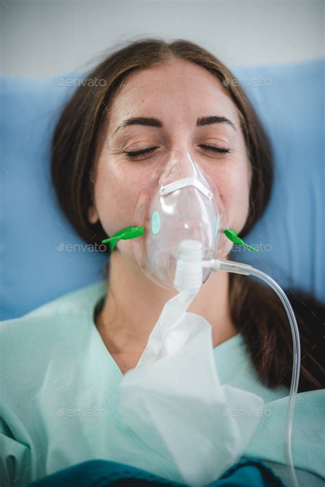 young woman patient receiving oxygen mask lying on a hospital bed ...