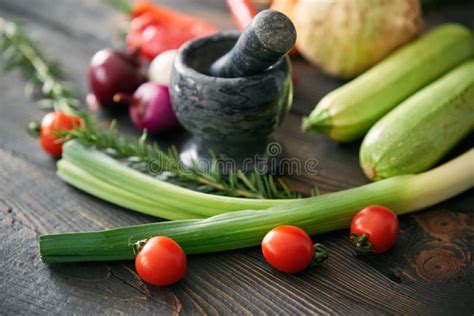Background with Assorted Raw Organic Vegetables and Black Marble Mortar with a Pestle on Wooden ...
