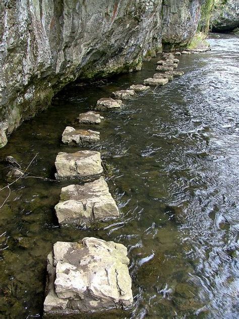 stepping stones are lined up along the edge of a body of water near a cliff