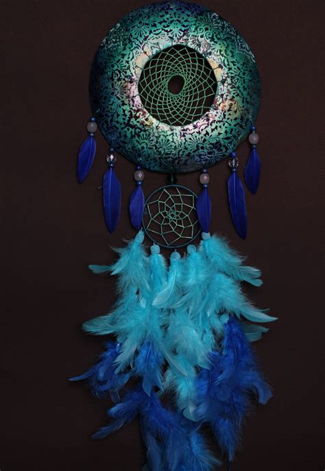 a green and blue dream catcher with feathers on it's side, against a black background