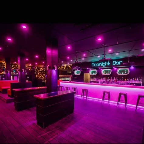 the bar is lit up with purple lights and wooden flooring, along with stools
