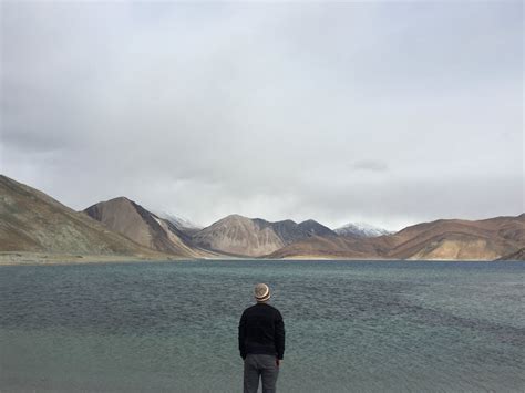 Person Standing Facing Body of Water With Hills at Distance · Free Stock Photo