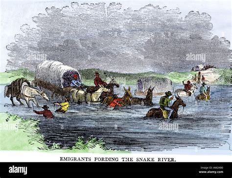 Pioneer covered wagon fording the Snake River on the Oregon Trail 1800s. Hand-colored woodcut ...