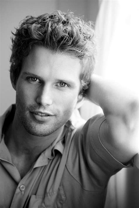 black and white photograph of a man with curly hair wearing a button up shirt looking at the camera