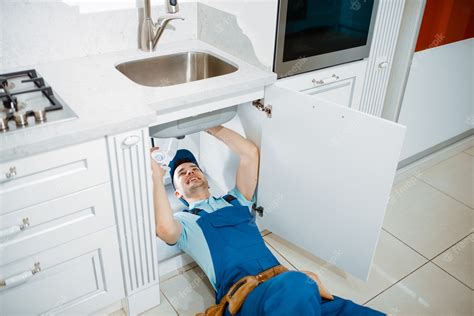 Premium Photo | Male plumber in uniform installing drain pipe in the kitchen. handywoman with ...