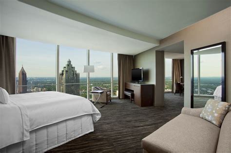 a hotel room with a bed, couch and large window overlooking the cityscape