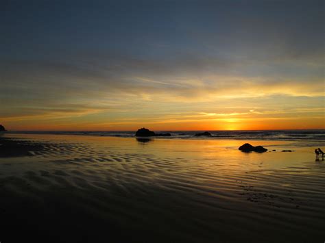 the sun is setting over the ocean with rocks in the foreground and ...