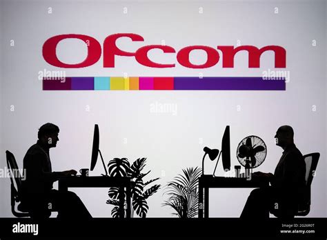 The Ofcom logo is seen on an LED screen in the background while two silhouetted people work in ...