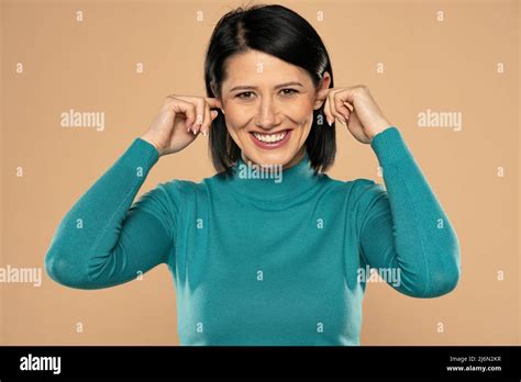 Middle aged happy woman plugging her ears with fingers on a beige background Stock Photo - Alamy