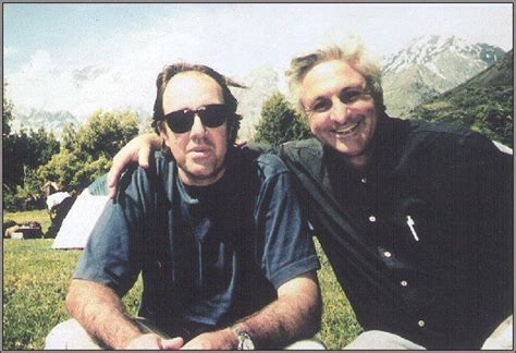 two men sitting next to each other on top of a grass covered field with mountains in the background