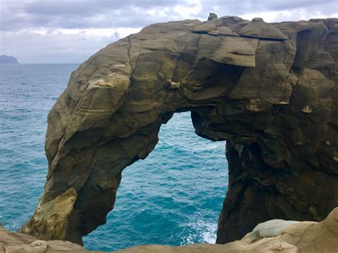 an arch shaped rock formation in the middle of the ocean with blue water behind it