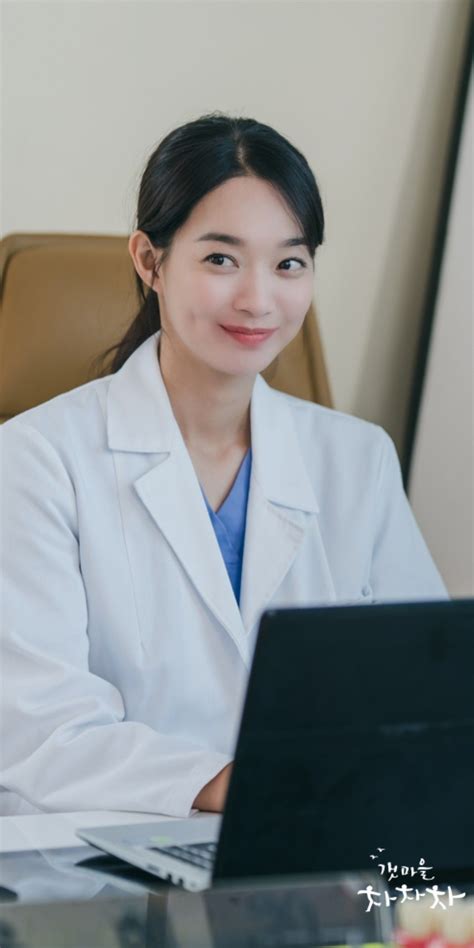 a woman in a lab coat sitting at a desk with a laptop computer on her lap