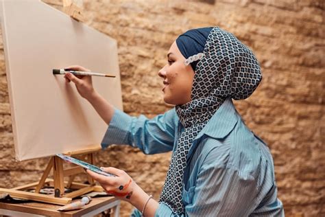 Premium Photo | A woman in a hijab paints on canvas with a brush and tempera