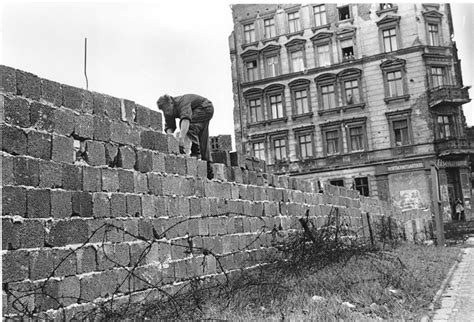 An East Berlin policeman puts bricks in place as the Berlin Wall is heightened to 15 feet, 5 m ...