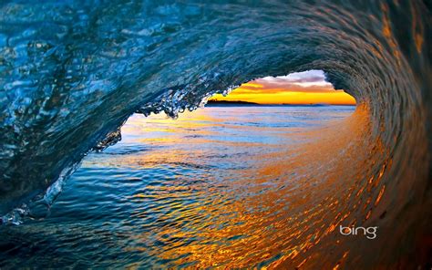 an ocean wave with the sun setting in the background