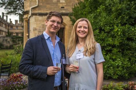 a man and woman standing next to each other holding wine glasses in front of a building