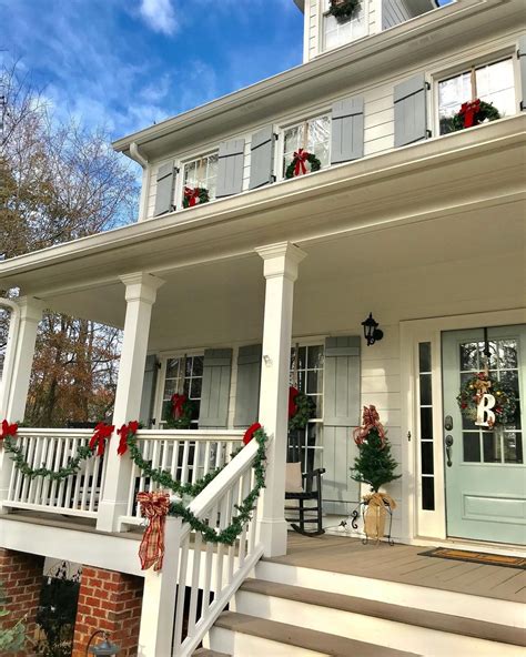 White farmhouse porch columns are joined together by matching railings draped with green garland ...