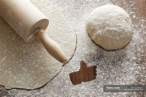 Closeup view of rolled-out pastry with a rolling pin, a ball of dough and flour with a like ...