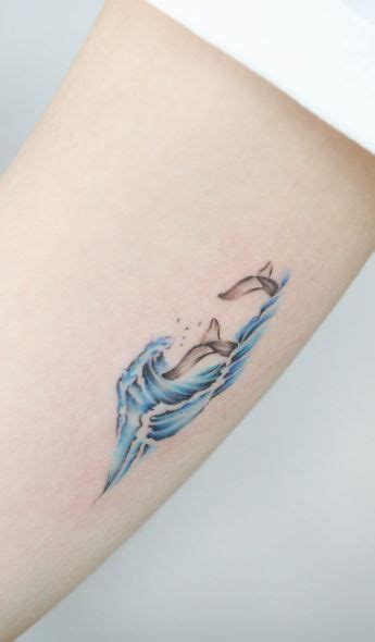 a woman's arm with a tattoo on it that has a dolphin in the water