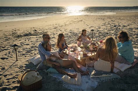 Family and friends enjoying picnic while sitting at beach during sunset. Riviera Nayarit, Mexico ...