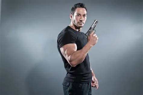 Action hero muscled man holding a rifle. Wearing black t-shirt w Stock Photo by ©ysbrand 47501519