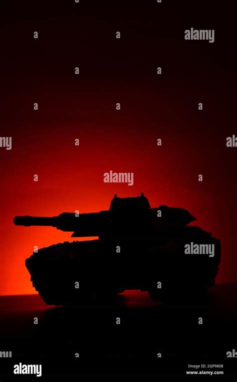 A military tank silhouette over a sunset background with deep red and orange hues which add ...