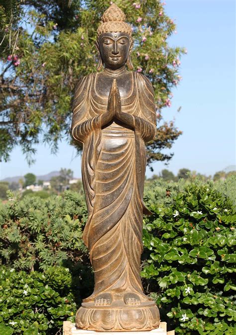 a buddha statue sitting in the middle of a garden with bushes and trees behind it