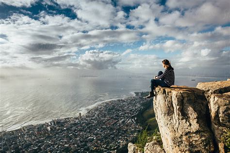 Woman sitting on the edge of a cliff overlooking Cape Town at sunset by ...