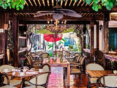 an outdoor dining area with tables, chairs and umbrellas hanging from the rafters